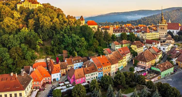 Luchtfoto van zonsopgang van Sighisoara's kleurrijke huizen verscholen tussen beboste heuvels.