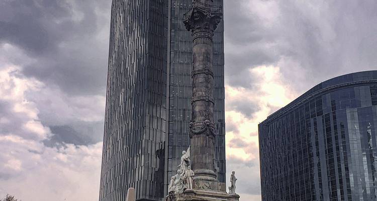 Le monument de l'Ange de l'Indépendance se dressant sur un ciel gris morose avec une tour moderne en arrière-plan.