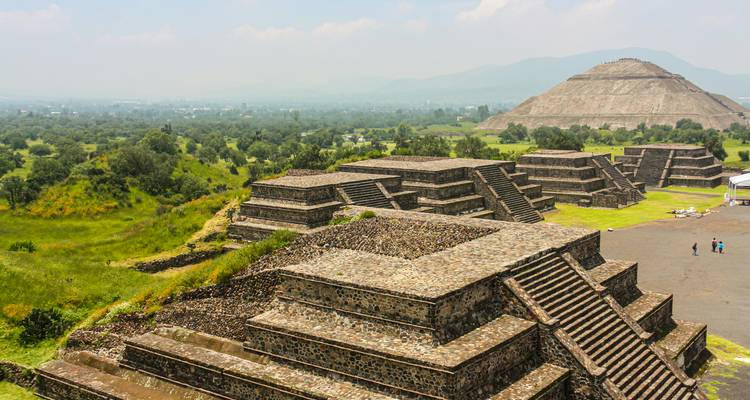 Vue panoramique sur les pyramides et les plateformes en gradins de Teotihuacán entourées d'un paysage de vallée verdoyante.