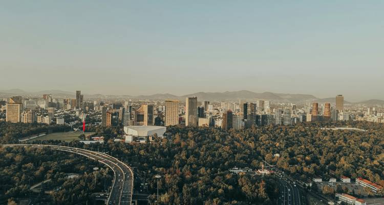 Skyline aérien de Mexico avec la verdure du parc de Chapultepec au premier plan et les montagnes lointaines.