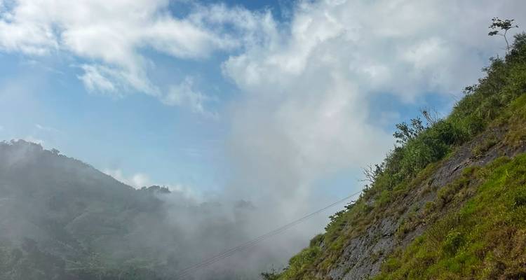 Fog rolling over lush green mountainside under partially blue sky