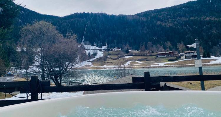 Whirlpool im Freien, sprudelnd mit ruhigem See, Wäldern und schneebedeckten Alpenhügeln in der Ferne.