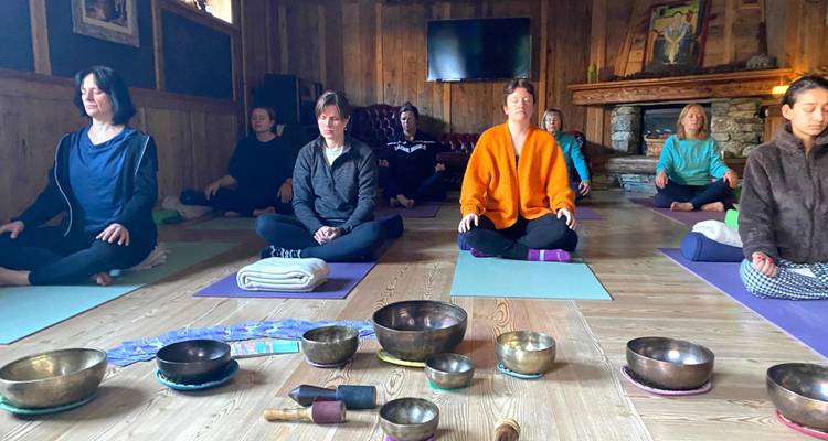 Eine kleine Gruppe sitzt im Schneidersitz auf Yogamatten in einem gemütlichen Holzstudio zur Meditation.