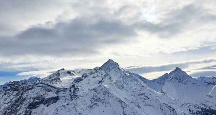 Dramatische, schneebedeckte Alpengipfel ragen in einen bewölkten Winterhimmel empor.