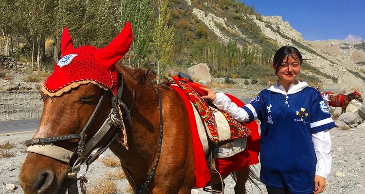 Jeune fille souriante se tenant à côté d'un cheval décoré avec des montagnes rocheuses et des arbres en arrière-plan.