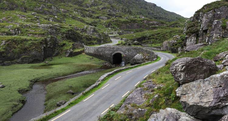 Route de montagne sinueuse traversant un vieux pont en pierre dans une vallée verdoyante luxuriante sur l'Anneau de Kerry