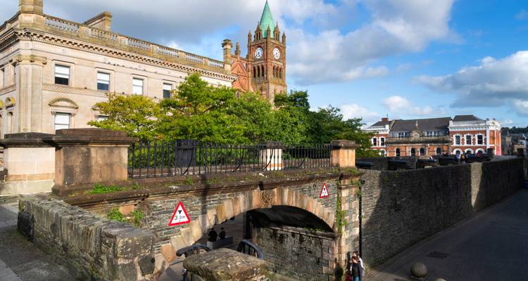 Historic stone walls and the red-brick clock tower of Derry’s Guildhall under a bright sky