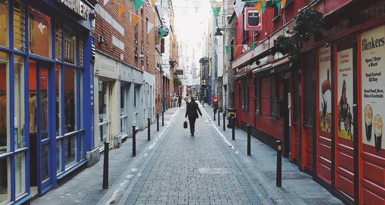 Narrow cobblestone street in Dublin lined with colorful shops and flags as a lone pedestrian walks away.