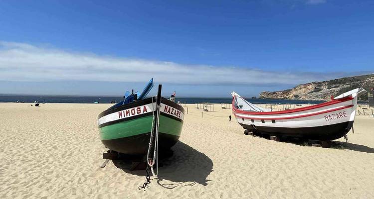 Les barques de pêche traditionnelles en bois reposent sur la vaste plage de sable de Nazaré sous un ciel bleu dégagé.