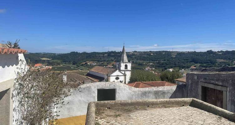 Vue sur un village portugais rural avec un clocher d'église et des terres agricoles en patchwork sur des collines ondulantes.