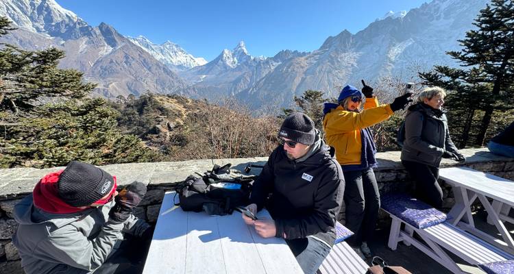 Wandelaars ontspannen zich aan picknicktafels buiten terwijl sneeuwtoppen in de verte uittorenend boven hen uittorenen.