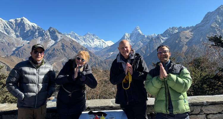 Vier glimlachende trekkers poseren met het traditionele namasté-gebaar tegen een Himalaya-achtergrond.