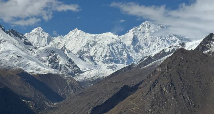 Sneeuwwitte Himalaya-pieken steken boven ruige bruine valleien uit onder een stralend blauwe hemel.