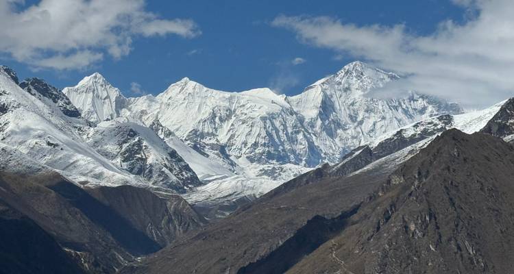 Helder uitzicht op glinsterende witte Himalaya-toppen in contrast met donkere rotsachtige voorgrond-berggraten.