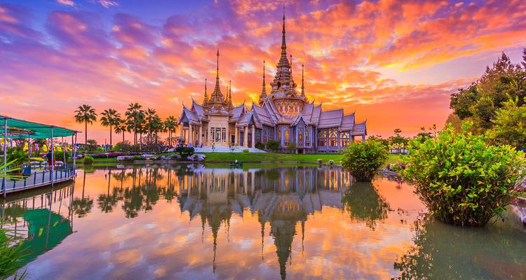 Complexe de temple thaï orné se reflétant dans un étang calme sous un ciel de coucher de soleil vibrant.