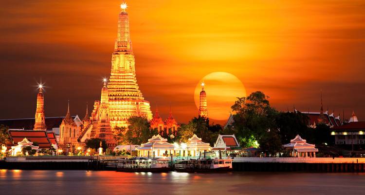 Le temple Wat Arun illuminé par un coucher de soleil orange dramatique avec le soleil se couchant derrière lui sur la rivière Chao Phraya.