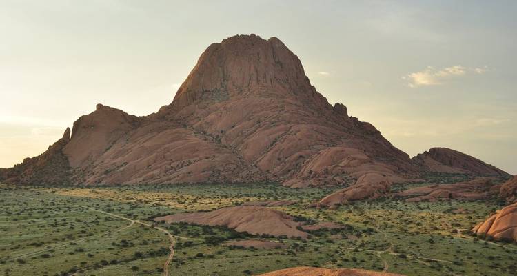 Un áspero pico de granito rosa se eleva sobre las llanuras desérticas escasas bajo la suave luz del atardecer.