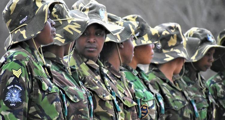 Unidad femenina contra la caza furtiva de pie en uniformes de camuflaje y sombreros de cubo, alineadas en formación.