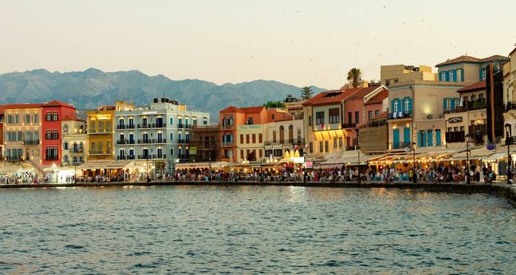 Waterfront promenade of colorful Venetian-style buildings at dusk beside calm bay.