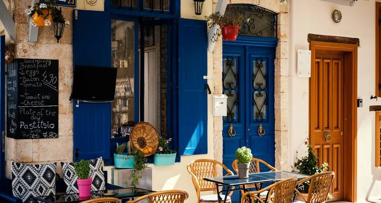 Outdoor café scene with blue doors, potted flowers and menu board on sunny Greek street.