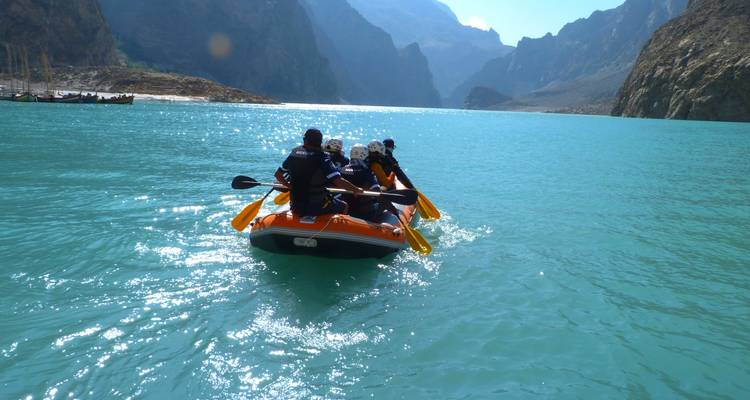 Raft glides over turquoise lake framed by dramatic jagged mountains under clear skies.