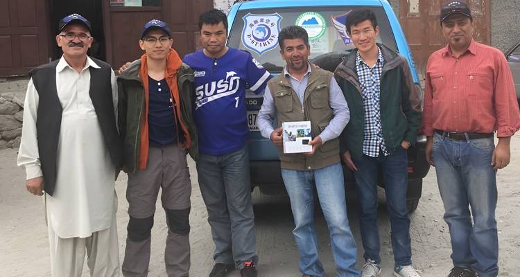 Group poses in front of a blue patrol truck after an outdoor adventure in a mountain village.