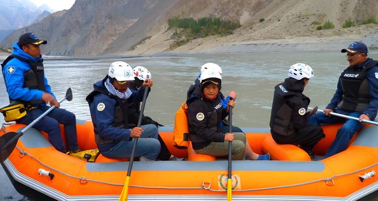 Adventure group rows together in an orange raft on a grey mountain river.