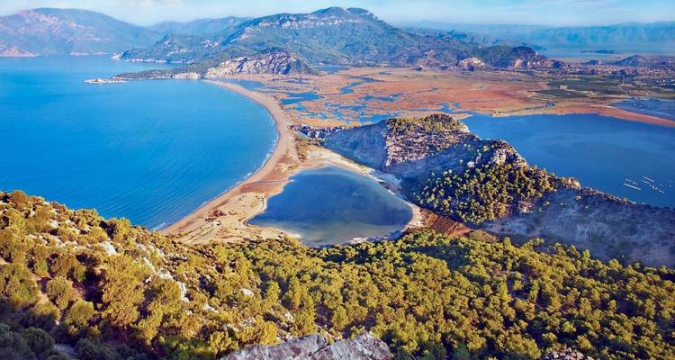 Verheven panorama van een uitgestrekt deltagebied met lagune, strand en omringende bergen.