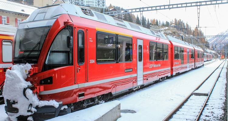 Train alpin rouge éclatant à une gare enneigée prêt pour un voyage panoramique en montagne.