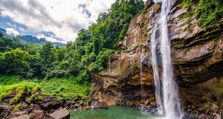 Cascade majestueuse se jetant dans un bassin verdoyant entouré de falaises recouvertes d'une dense forêt tropicale.