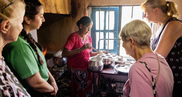 Une femme locale démontre la cuisine traditionnelle sri-lankaise dans une cuisine rustique tandis que les voyageurs observent attentivement.