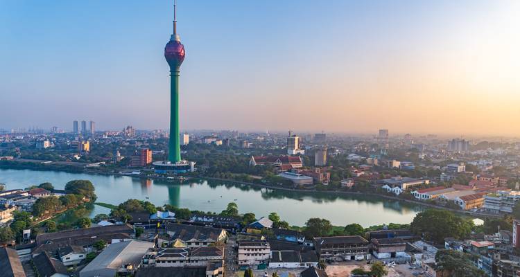 Panoramic view of Colombo skyline at sunrise featuring the Lotus Tower beside a reflective lake.