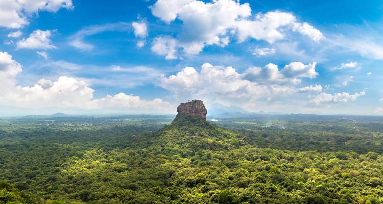 Aerial vista of Sigiriya Rock rising above an endless green jungle under a brilliant blue sky.