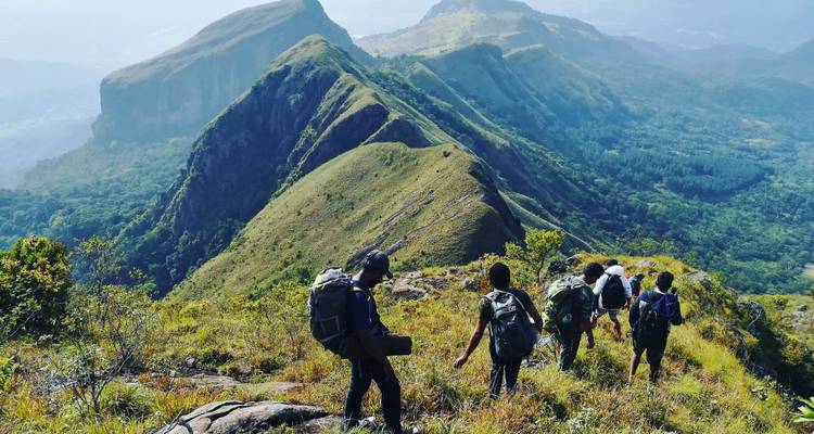 Hikers with backpacks traverse a razor-back ridge with sweeping mountain vistas.