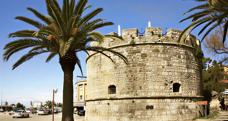 Circular Venetian tower of Durres framed by palm trees on a bright day.