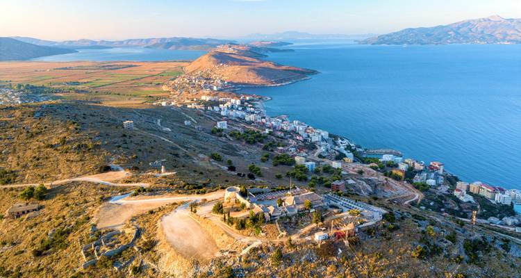 Vue aérienne du coucher de soleil sur la côte de Saranda et les îles de Ksamil avec des collines ondulantes rencontrant la mer Ionienne.