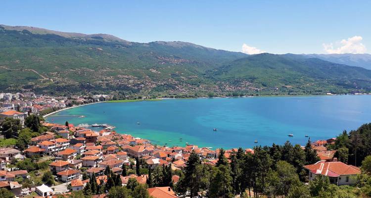 Vue panoramique des eaux turquoise du lac Ohrid et des toits en terre cuite sous des collines boisées.