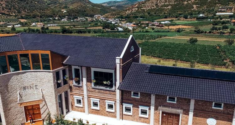 Complexe viticole moderne surplombant des vignobles en patchwork et une vallée rurale albanaise.