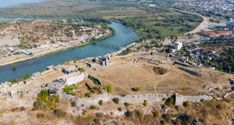 Vue aérienne d'une forteresse historique sur une colline dominant une rivière et des ponts en contrebas.