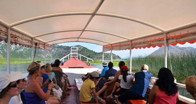 Les touristes assis sous un auvent profitent d'une excursion en bateau décontractée à travers les roseaux du lac de Skadar.