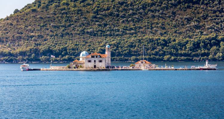 Île longue et étroite avec église et chapelle dans la baie de Kotor entourée d'eaux d'un bleu profond.