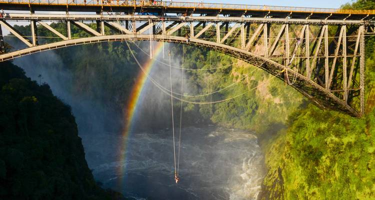 El histórico puente de las Cataratas Victoria con arco iris en el arco y líneas de bungee sobre el desfiladero furioso