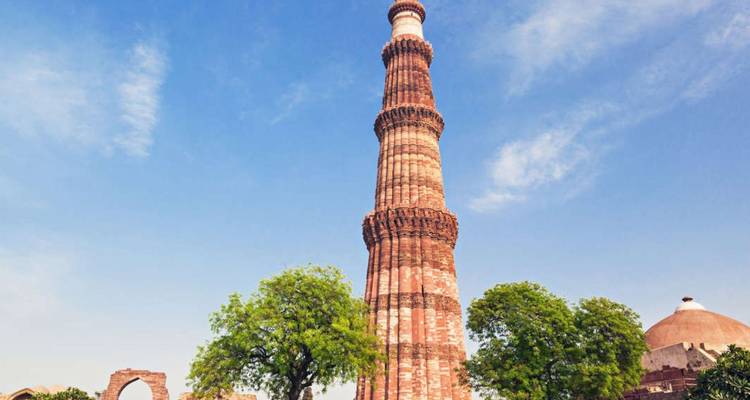 The soaring red-sandstone Qutub Minar towers against a clear blue Delhi sky.