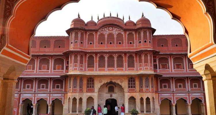 Visitors framed by an arched gateway admire the richly detailed City Palace in Jaipur.