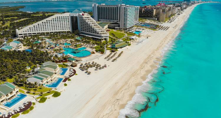 Drone view of Cancun hotel zone showing long white beach, turquoise surf and expansive resorts.