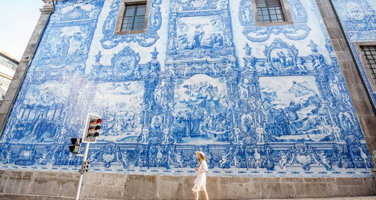 Jeune femme passant devant la façade élaborée de carreaux azulejo bleu et blanc de la Capela das Almas à Porto.