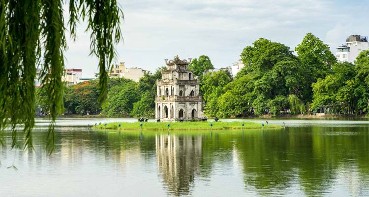 The ancient Turtle Tower sits on a small island in Hanoi’s Hoan Kiem Lake framed by foliage.