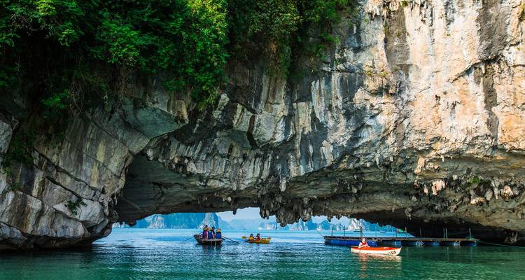 Karst archway towers above turquoise water as small boats navigate Halong Bay’s limestone formations.