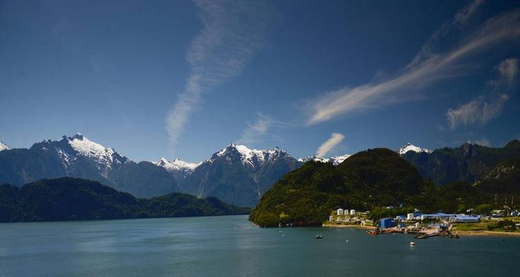 Les montagnes des Andes enneigées s'élèvent au-dessus d'un fjord calme sous un ciel bleu profond.