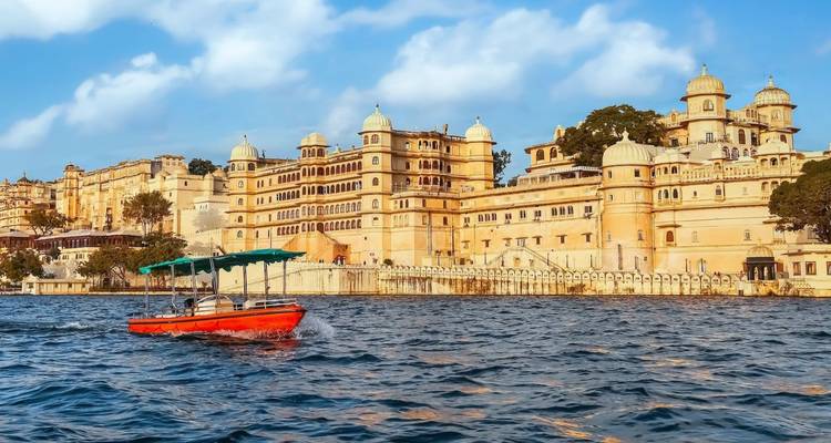 Het majestueuze City Palace complex domineert de oevers van het meer terwijl een rode boot over Udaipurs wateren vaart.
